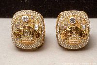 Front view of two gold-tone 2019 NBA Toronto Raptors championship replica fan rings with clear rhinestones and large center rhinestone