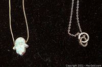 Close-up view of two silver necklaces pendant: one with opal Hamsa shape and one with interlocking ring design.