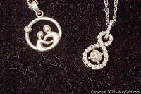 Close-up of two silver pendants showing design details on black fabric background.