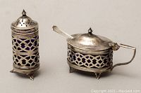 Two sterling silver pierced footed salt cellars with cobalt blue glass liners and small silver spoon shown from the front.