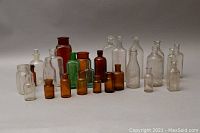 Group of 22 antique/vintage glass apothecary bottles in clear, amber, green, and brown colors arranged with some bottles having stoppers. Size varies from small to large.