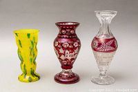 Front view showing three crystal vases: yellow with green spots, ruby red with etched designs, clear with ruby red floral band