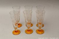 Six pilsner beer glasses arranged in inverted V shape showing clear bowls with etched cornflower pattern and amber yellow feet