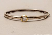 Front view of the sterling silver bangle with 14kt gold bezel holding a clear stone.