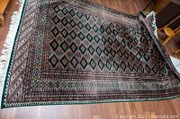 Full view of rug laid flat on wood floor showing overall pattern and fringed ends.
