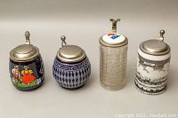 Four German beer steins side by side showing varied decorations, lids and finials
