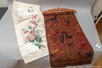 Both fabric wall hangings side by side on grey surface, showing silk textile and wooden carved rod