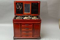 Large footed wooden jewelry box with lift-top open showing mirror, necklace hooks, drawers, minor nicks on box edges