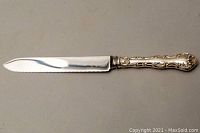 Full view of bread/cake knife showing serrated stainless steel blade and ornate silver handle