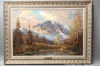 Painting showing full mountain and lake landscape with autumn trees, framed in ornate white carved wooden frame.