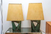 Pair of lamps side by side on glass-topped table against white wall.