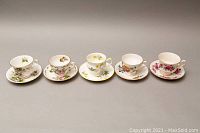 Front view of five porcelain teacups with matching saucers, all with floral patterns and gold trim details.