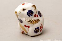 Front angle view of white porcelain mouse paperweight decorated with gold wheat leaves, blue floral designs, and red cherries