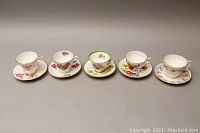 Front view of five teacup and saucer sets showing various floral patterns and gold rim detail.