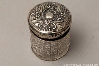 Front view of sterling silver lidded vanity jar showing detailed ornate lid and cut glass body.