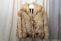 Front view of the curly alpaca fur jacket, beige with brown shades, detailed texture and toggle closure.