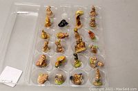 Photo shows all 23 assorted miniature figurines arranged in a clear plastic storage tray with compartments.