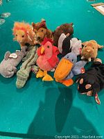Image displaying a group of 10 Ty Beanie Babies plush toys on a green surface. Various animal characters visible including lion, dog, rooster, pelican, and others.