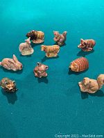 Top-down view of 10 Wade Whimsies ceramic animal figures on teal surface including fox, rabbit, raccoon, armadillo, llama, sheep, cow, bear, and squirrel.