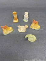Photo of six ceramic figurines from the front, showing boot, clock, animal, and reptile designs.