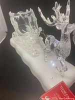 Photo showing the front and side of the clear acrylic reindeer pulling a sleigh on a white base with LED lights.
