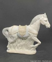 Side view of ceramic horse figurine showing flowing tail, saddle, and textured base