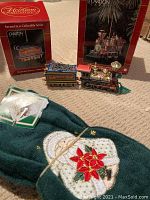 Overview of the Wonderland train engine and coal car ornaments next to the two holiday fingertip towels on carpeted surface.