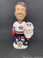 Front view of Ed Belfour bobblehead in Team Canada hockey gear, holding goalie mask and showing gold medal base.