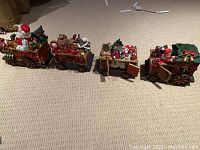 Four resin Christmas train cars with Santa on the engine and other festive figures. Train is posed on carpeted floor showing its size and details.