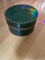 Closed solid round container showing green exterior and metal stud detailing