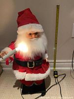 Santa Claus figurine holding a lit candle-style light, shown with tape measure for scale indicating about 2 feet tall.