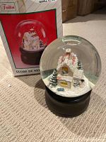 Glass snow globe with snowy house scene inside and original box visible behind