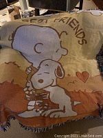 Blanket with Snoopy hugging Woodstock and 'Best Friends' text, beige and brown tones.