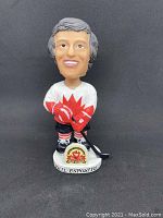 Front view of Phil Esposito bobblehead in white hockey jersey with red maple leaf and holding hockey stick.