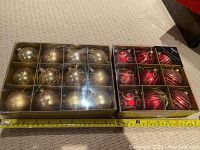 Two boxes of shatterproof plastic Christmas ornaments: one box contains smooth sparkly gold ornaments, the other box contains red ornaments with glittery swirls and stripes. A measuring tape is shown for scale.