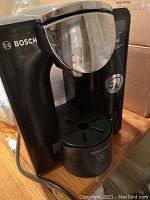Front view of the Bosch Tassimo coffee machine highlighting the glossy dispenser, Bosch logo, and pod insertion area with drip tray.
