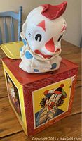 Front view of clown's head popping out of the box, showing molded plastic head and fabric shirt with some wear