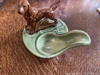 Photo showing the pipe holder with a brown dog figurine attached to a green base, placed on a wooden surface.
