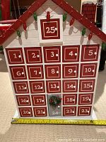 Front view of the wooden advent calendar house with numbered doors 1 to 25 and decorative string lights on roof.