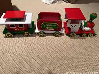Full view of three-piece wooden Christmas-themed toy train set laid out on carpeted floor.