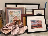 Overall view of the grouped framed art and photography pieces stacked against a wall.