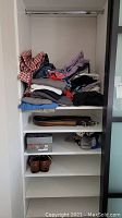 Image of folded men's clothing including shirts and jeans on shelves with belts and shoes below.