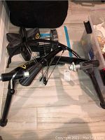 CycleOps black indoor bike trainer folded on floor with visible roller resistance assembly and legs.