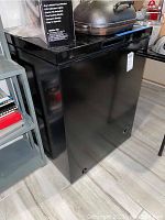 Front view of black upright Arctic King freezer with visible brand logo and top lid handle.