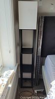 Pair of two black floor lamps with white rectangular shades and vertical shelving units, positioned next to bed and window.