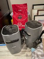 Two grey Litter Genie cat litter disposal units with black lids and a large red bag of World's Best Cat Litter behind them, along with visible white cat litter pads in background.