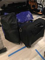 Black rolling suitcase and blue bags on floor with additional equipment in background