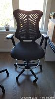 Front view of black office chair showing mesh back, cushioned seat, armrests, and wheeled base with foot ring.