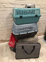 Photo of stacked teal and gray plastic pet carriers, bag of cat litter, and gray collapsible fabric cat playpen with black handles