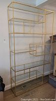 Full front view of gold-tone metal étagère showing asymmetrical open shelving